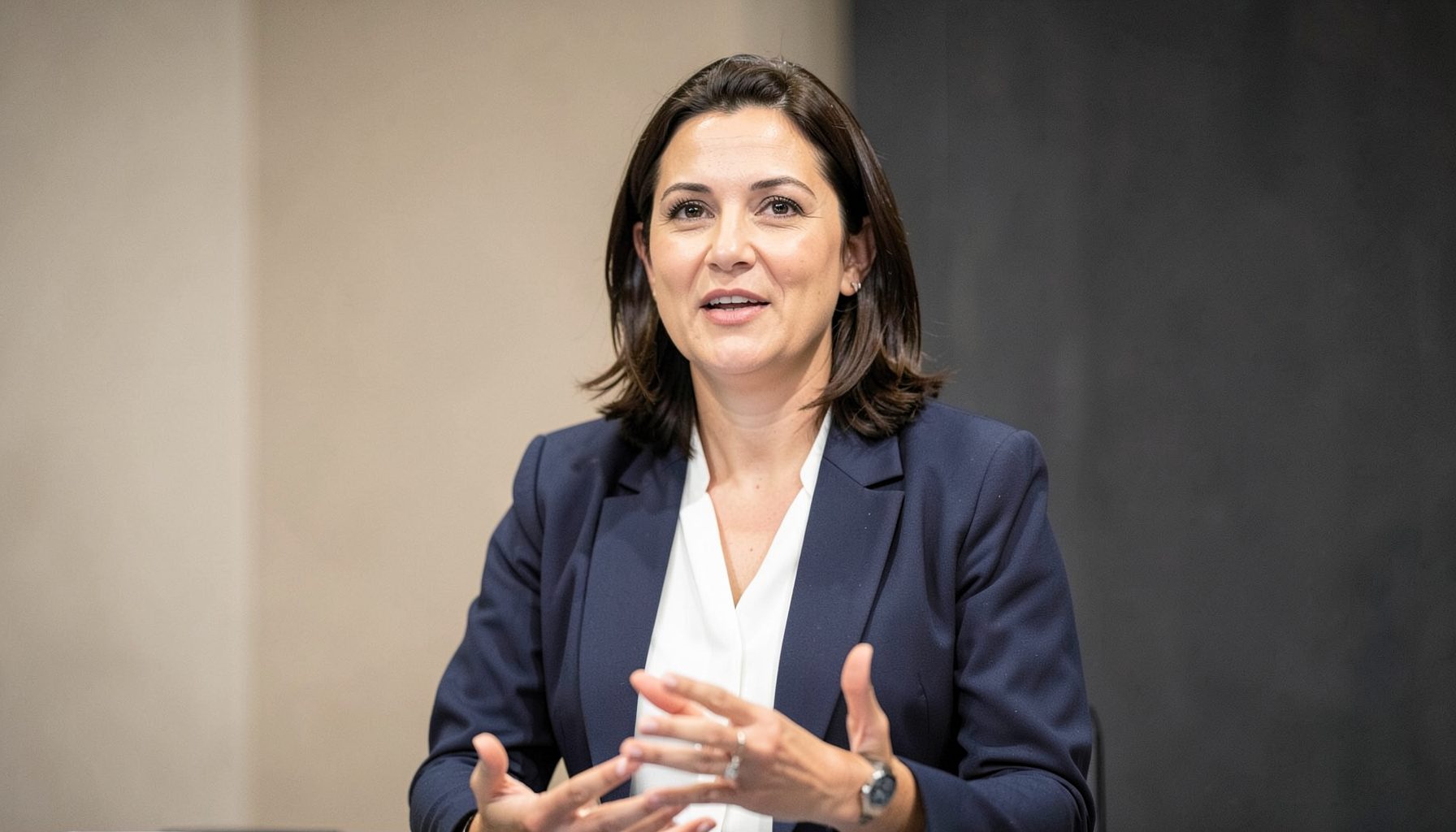 A confident woman speaking at a leadership forum, poised and articulate, soft natural lighting with neutral beige and charcoal tones