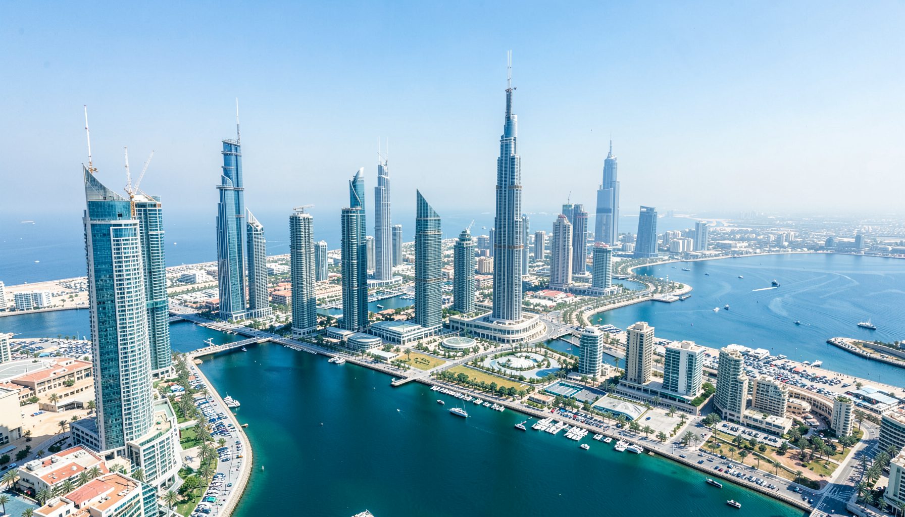 Aerial cityscape view of the Business Bay district in Dubai with modern high-rise towers, blue waterways, and clear sky